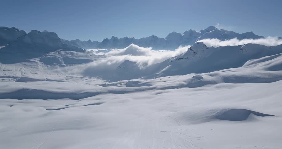Clouds are drifting across snow-covered mountain peaks on a sunny day