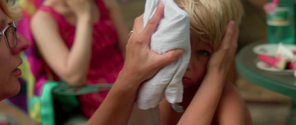 An adult is putting a cold compress on a boy's head outside in summer