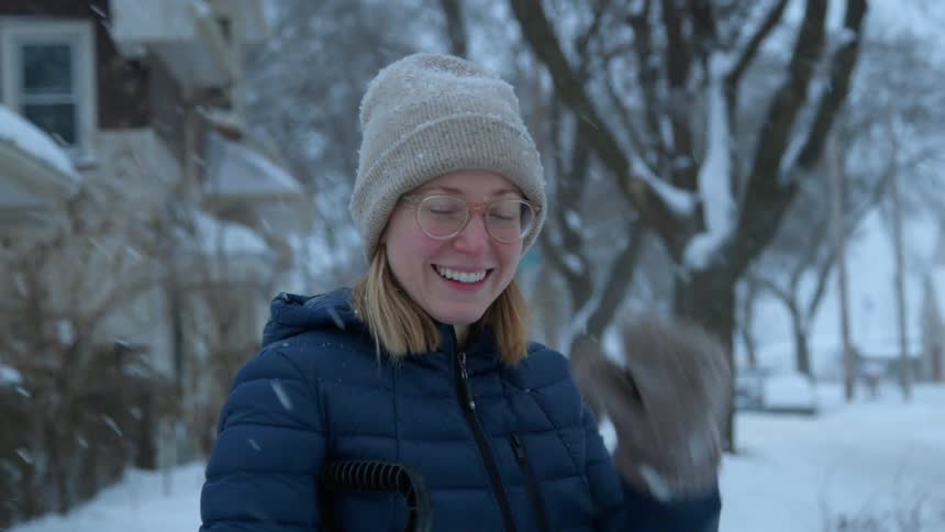 Bespectacled woman smiling outdoors while it's snowing