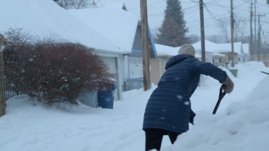 Woman shovels snow from a sidewalk
