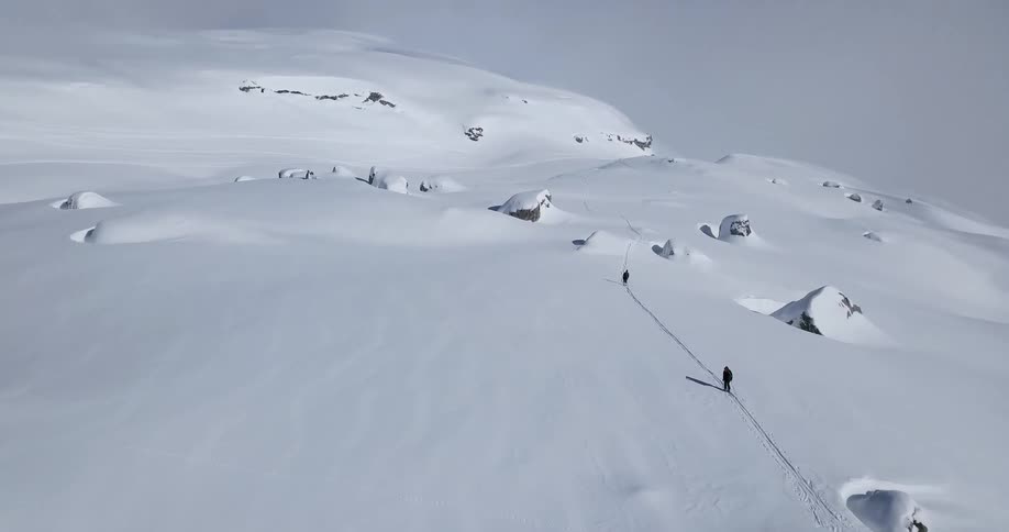 Two people walk up a snowy mountain