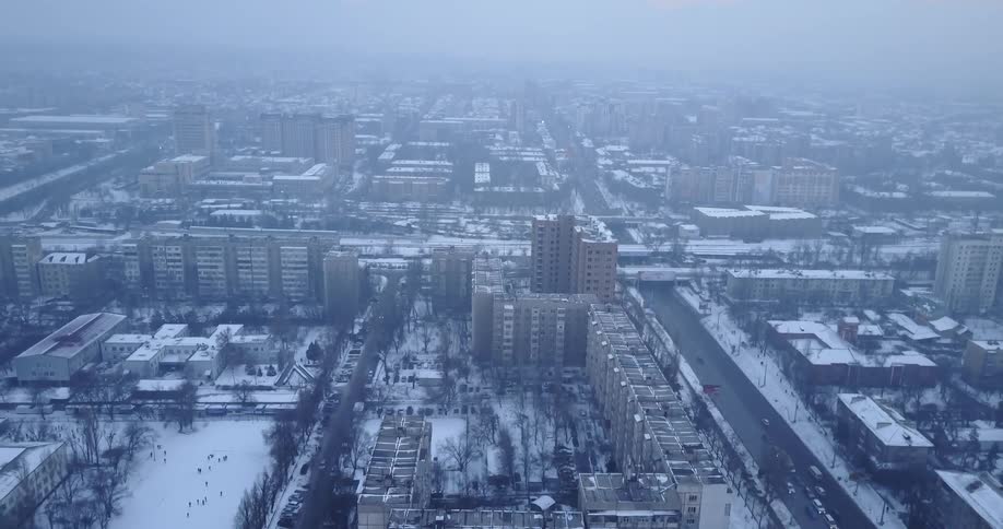Cars drive by snowy city buildings