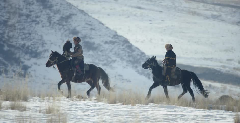 Men ride horses with a hunting eagle