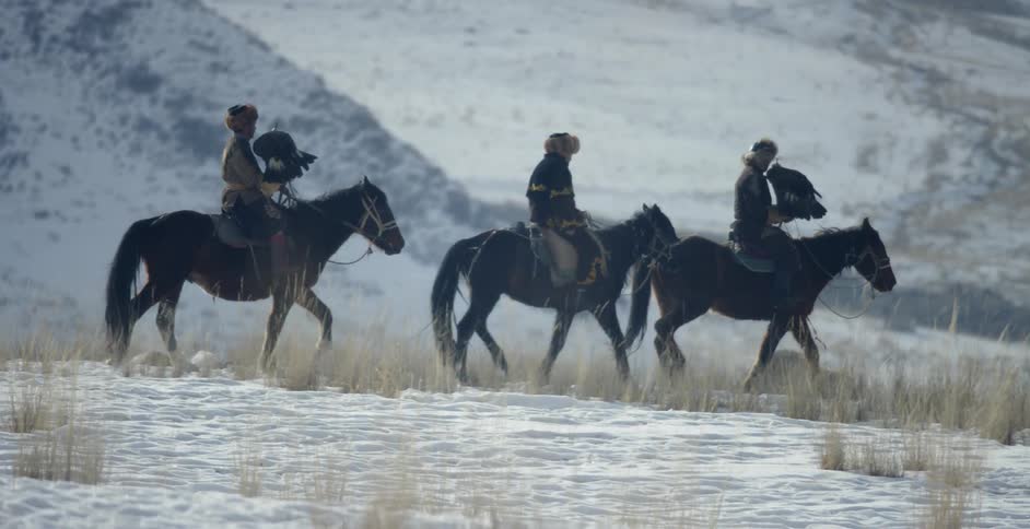 Three men ride horses while holding large birds