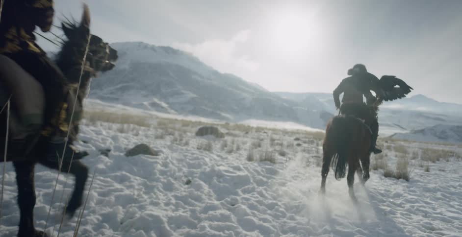Men ride horses across snow with hunting eagles