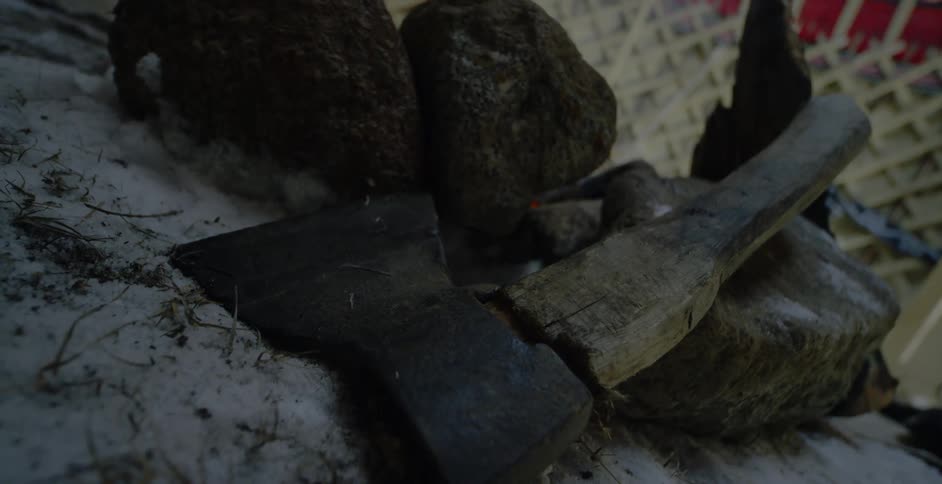 An ax lies in the snow near stones around a fire