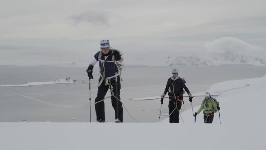 Group of people hike up a snowy mountain using poles and a rope
