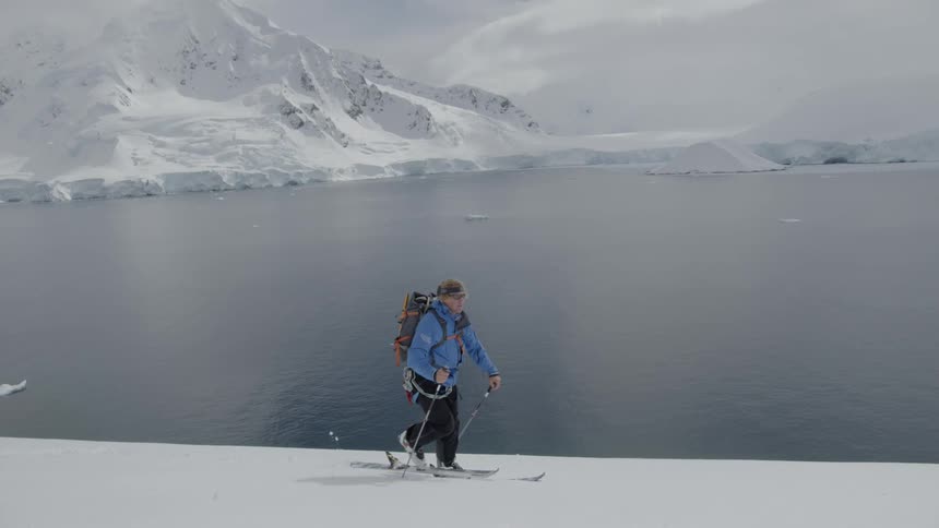 A man is hiking along the snow by the lake