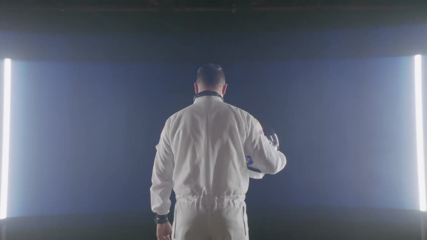 A man in a white space suit stands in front of lights