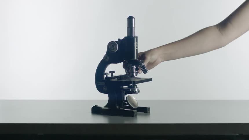 Person's hand reaches out and turns a microscope