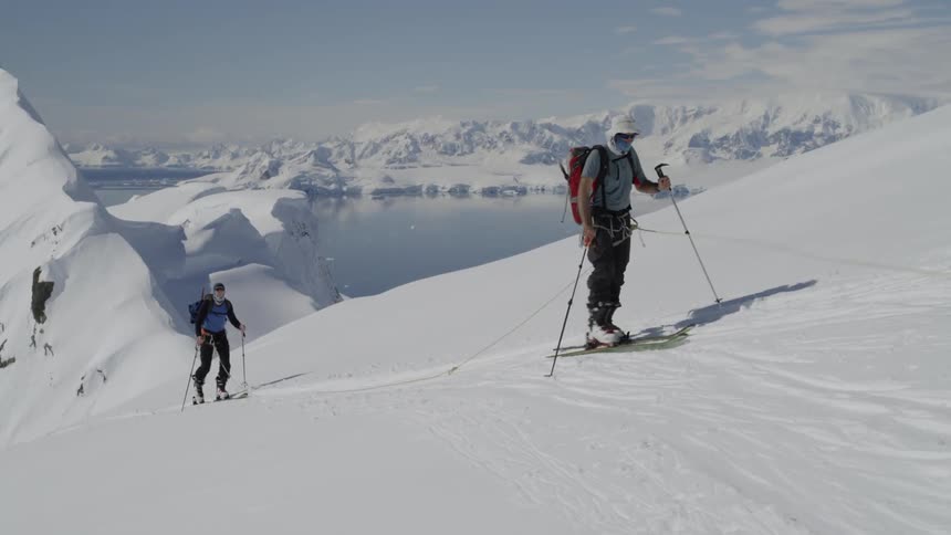 Two people wearing skis use poles to walk up a snowy mountain