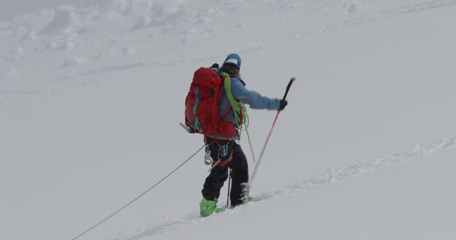 Man skis up the side of a mountain as he pushes himself with his poles
