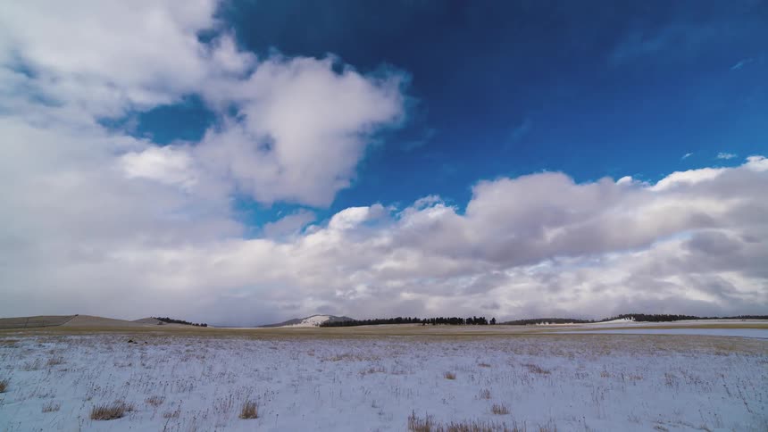 Fluffy clouds float over a field covered with a light layer of snow