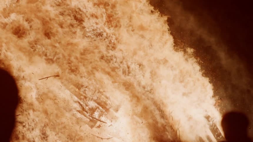 People watch as a structure on fire collapses