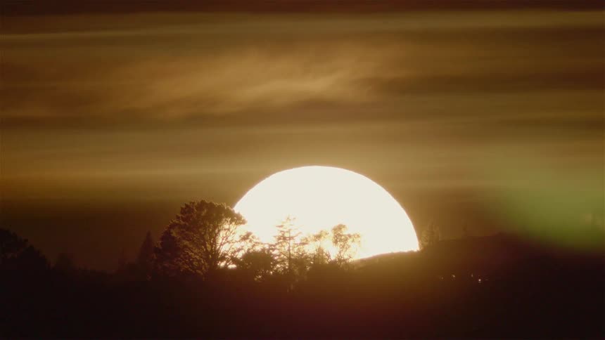 The sun sets behind a hill and trees