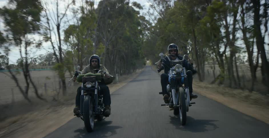 Two men ride motorcycles on a rural road