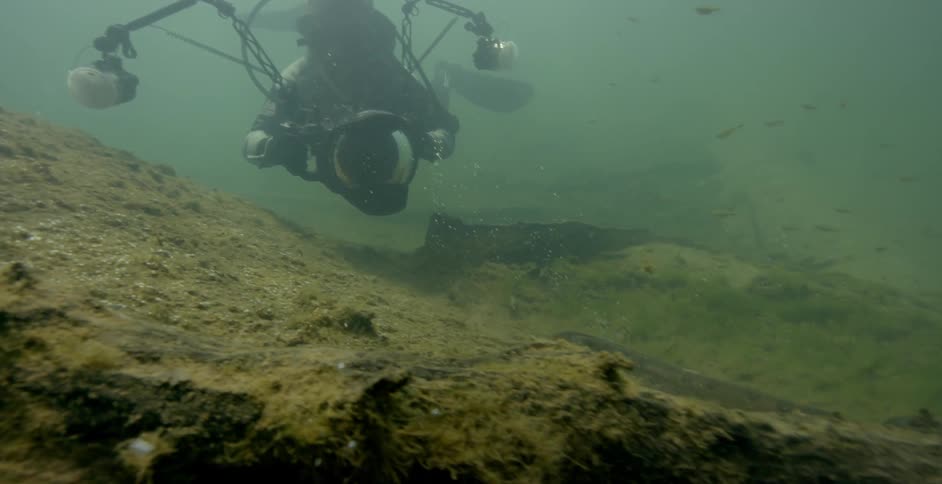 The diver moves through the murky waters with a camera