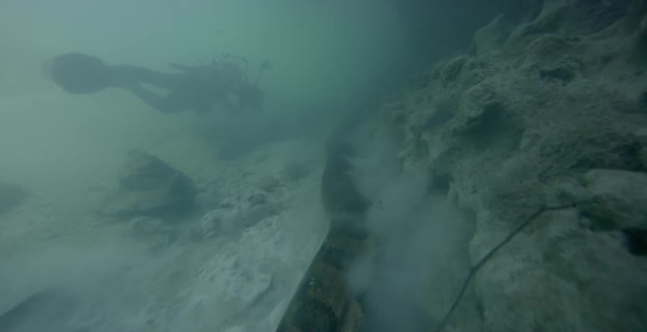 A scuba diver photographs a large snake moving along the sand
