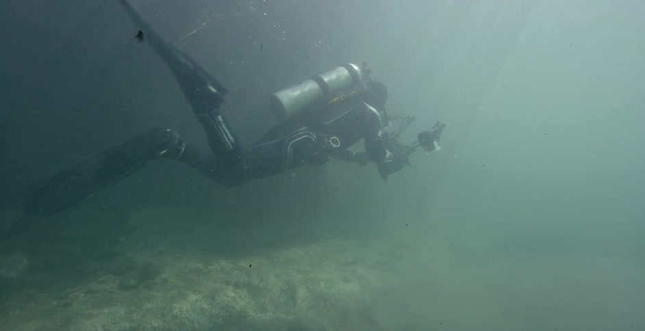 Diver swims in murky water carrying recording equipment