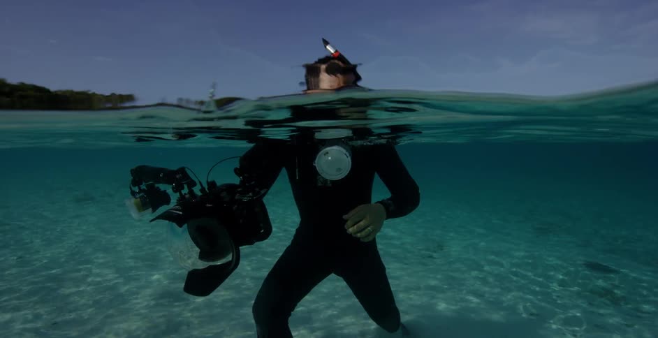 A diver walks around in the shallow water with a camera
