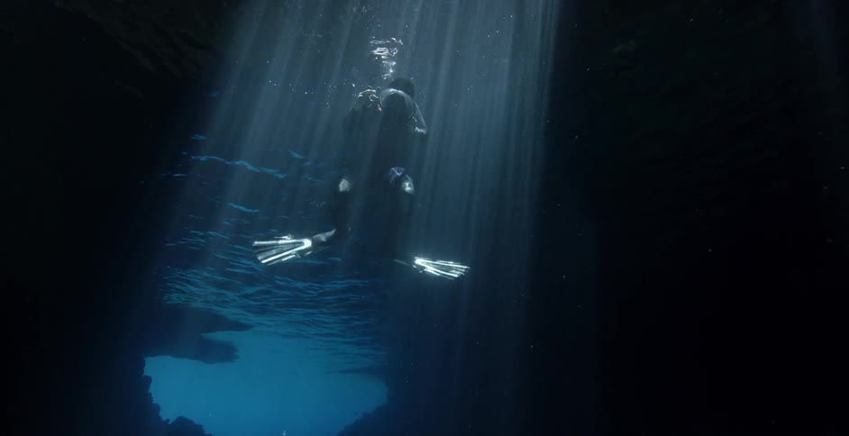 A diver is descending into an underwater cavern while holding a camera