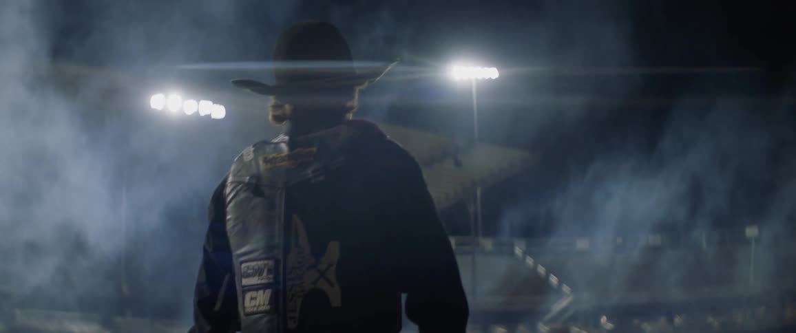A cowboy walks through a well lit arena