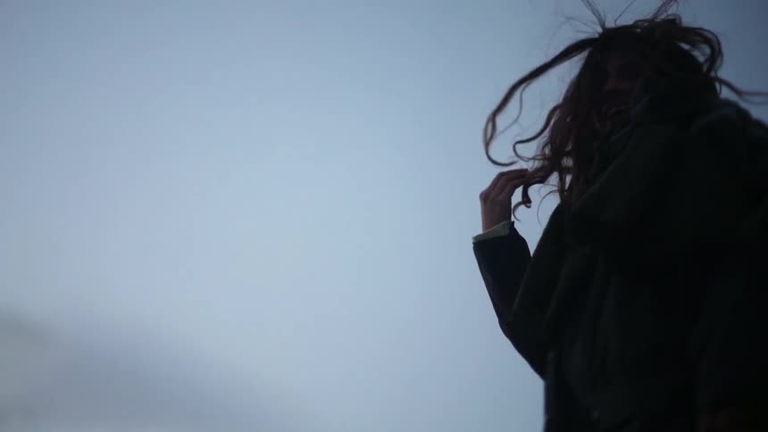 The wind is blowing a woman's hair as she stands outside at dusk