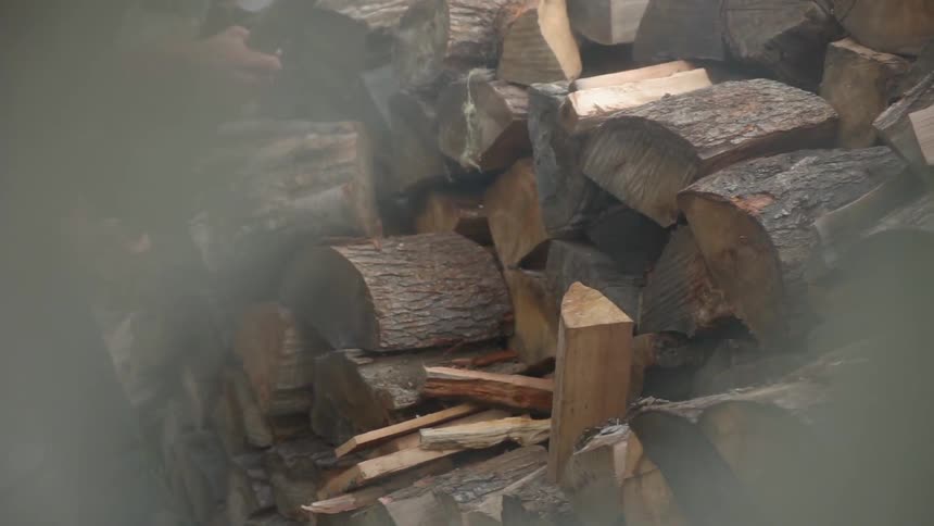 A man is splitting wood logs outside in daylight
