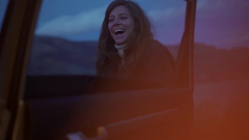 Woman smiles and laughs outside by a car door