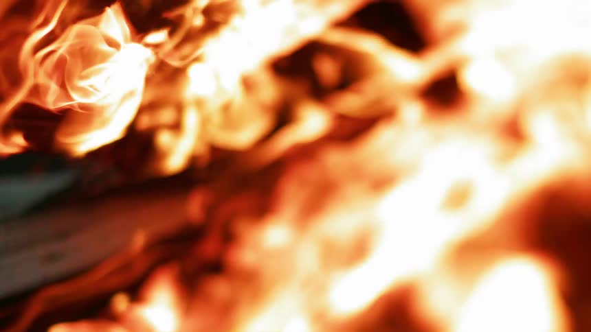 Flames are swirling around wood boards in a bonfire at night