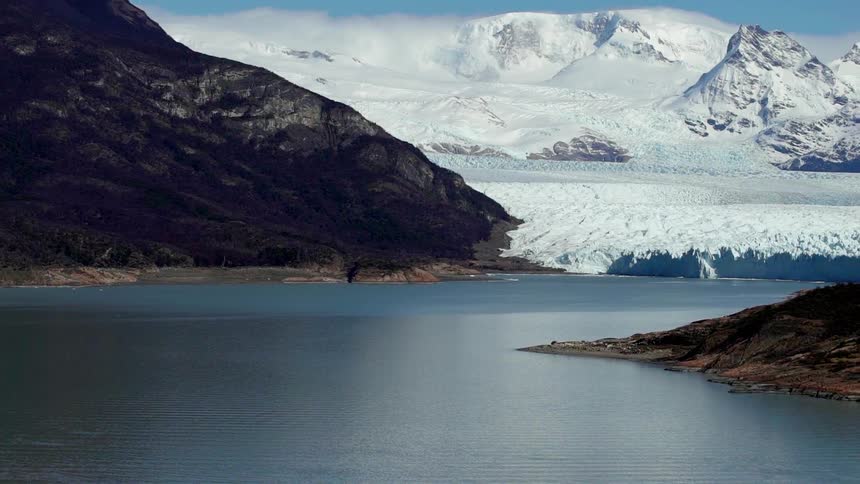 Snow covered slope leads to a lake surrounded by hills