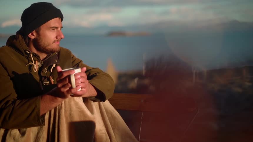 A man holds a hot cup in his hands while sitting on a deck