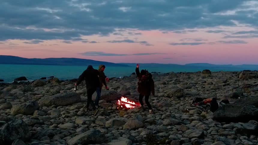 People run around a lakeside bonfire at sunset