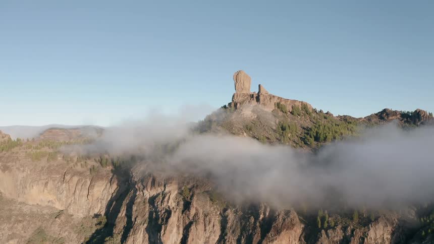 Clouds are drifting across a mountain with a rock formation on a sunny day