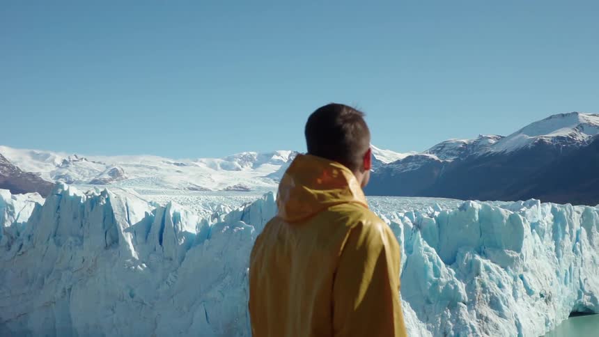 A man looks around at an iceberg on a sunny day
