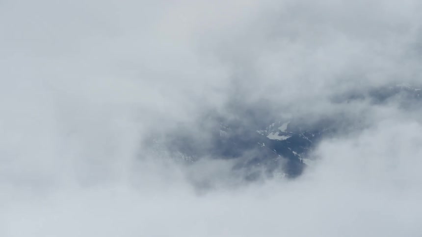 Clouds are drifting over a snow-covered mountain range in daylight