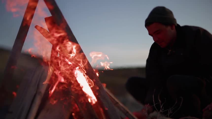Man stands outside close to a fire at sunset