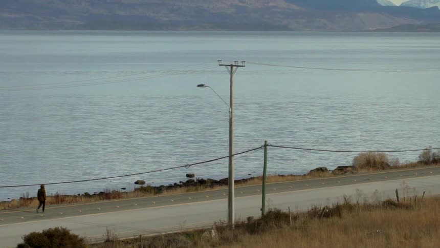 Person walks on the side of a road near a large body of water