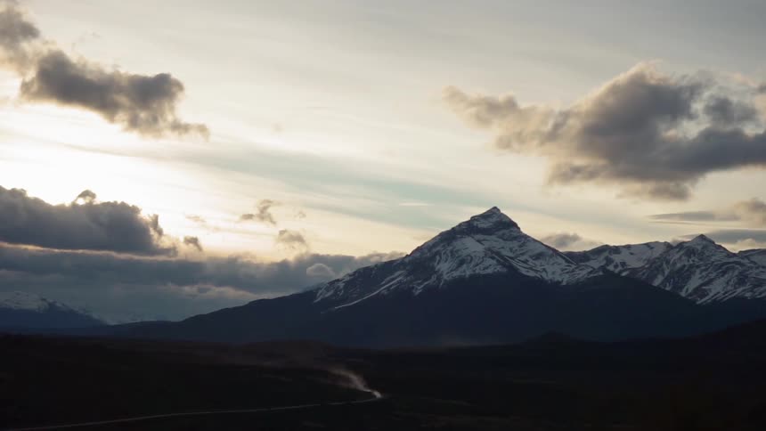 Clouds float over snowy mountains at sunset