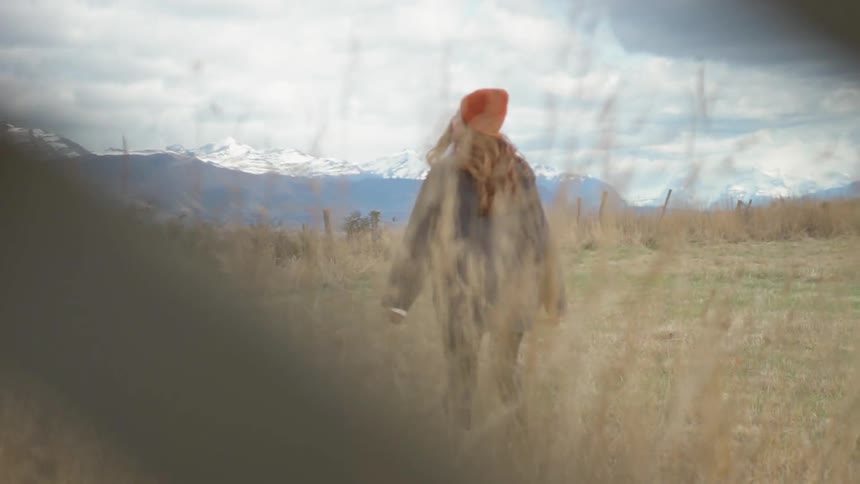 A woman is walking away from a vehicle into a field on a cloudy day