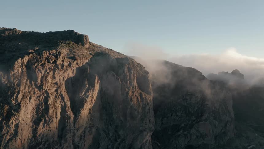Clouds float around rocky mountains