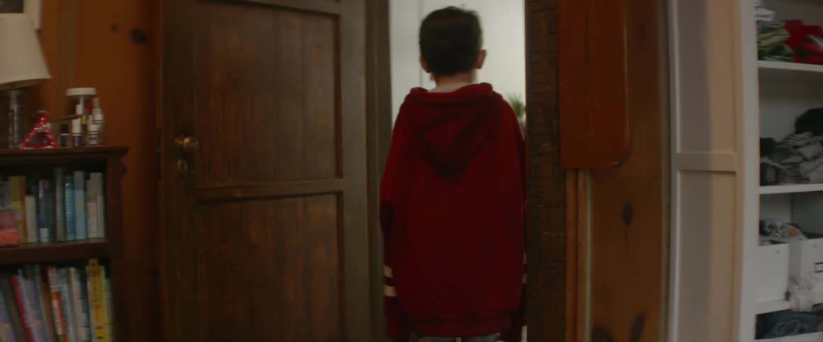 A boy in an oversize sweatshirt walks through a doorway into another room