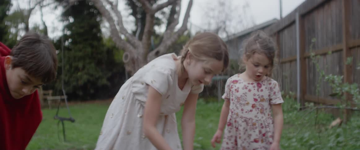 Three children are playing in a backyard garden in daylight