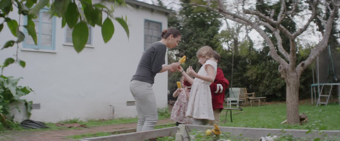 A mother is bringing her children popsicles in a backyard during the day