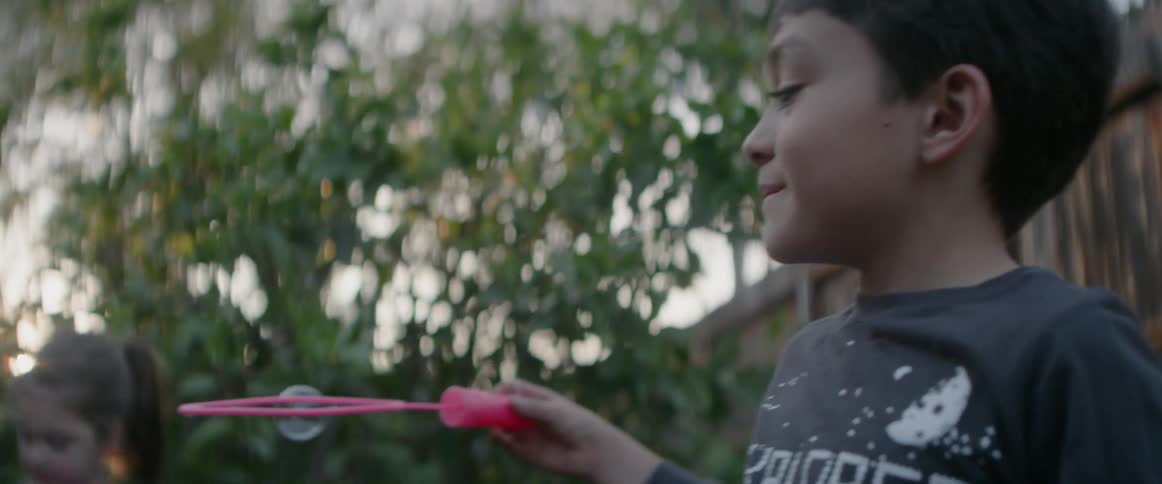 A boy is blowing bubbles in a backyard in daylight