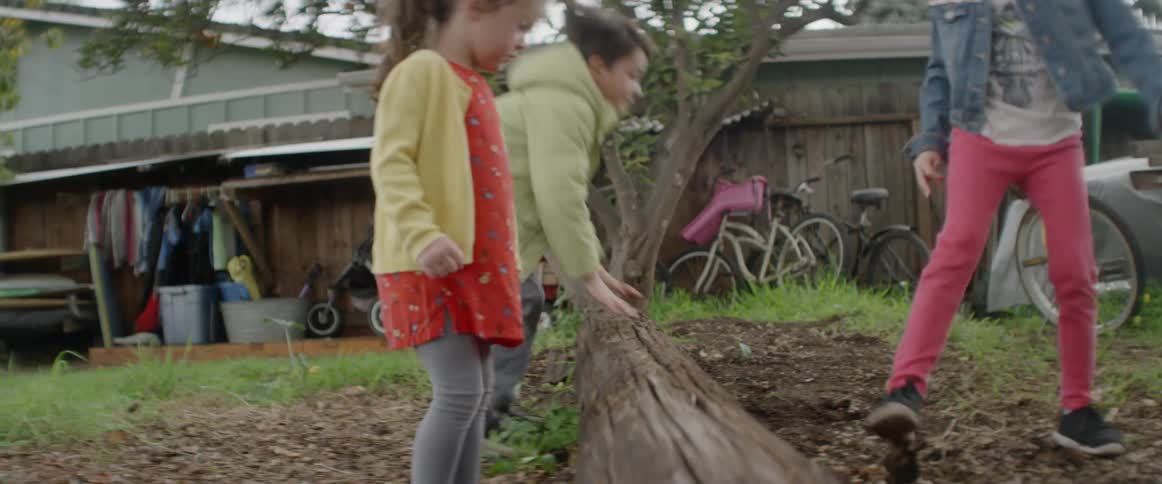 Kids jump over a log in a backyard