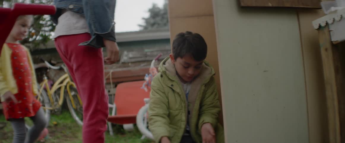 A girl grabs a toy from a boy as he takes it from a box outside in daylight