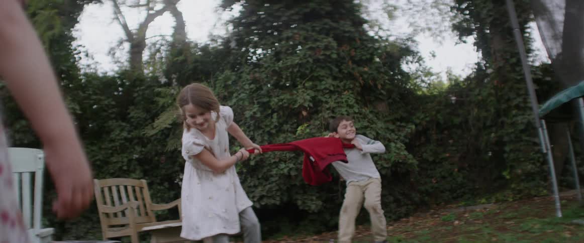 A boy and girl play tug of war with a jacket