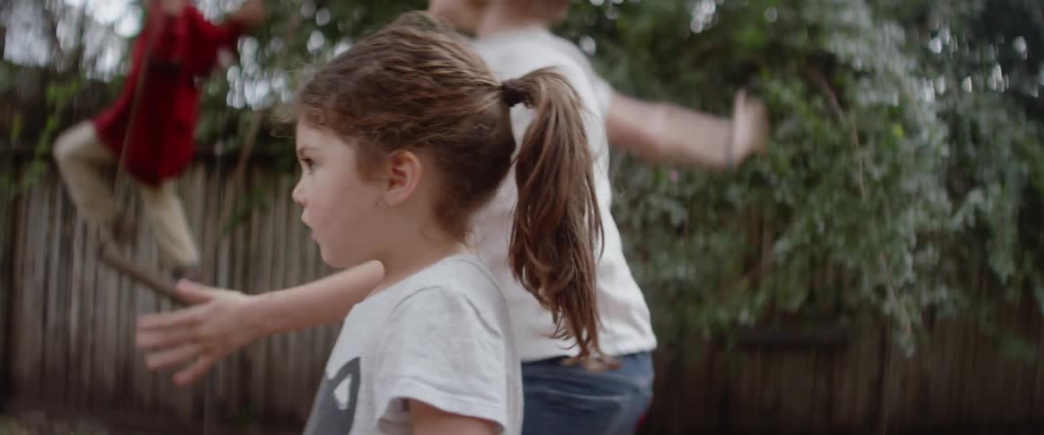 Three children playing in a backyard and one of them jumps off a swing