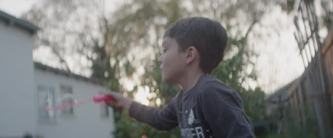 A boy is blowing bubbles in a backyard at dusk